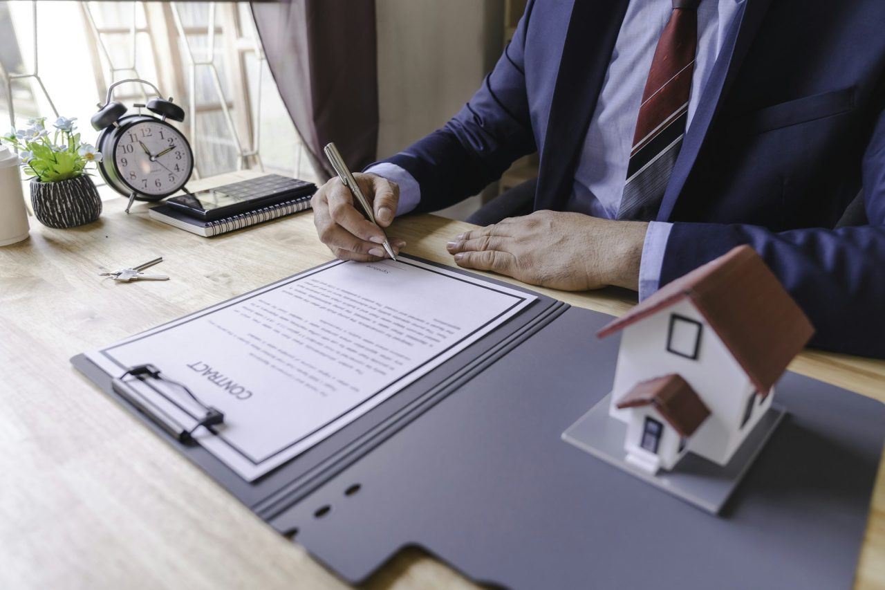 businessman signing signature loan document to homeownership mortgage and real estate property inve