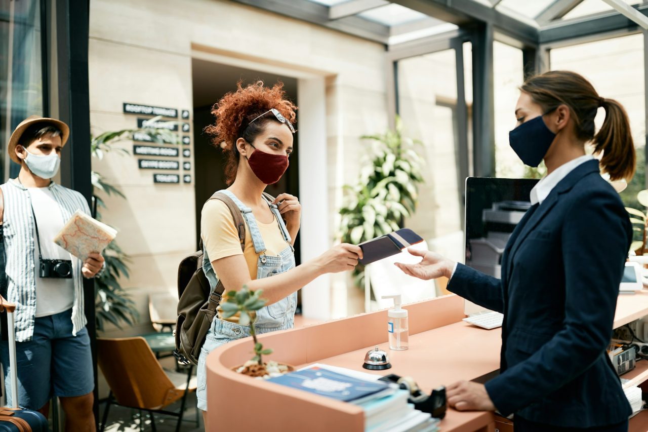 young woman wearing face mask during check in at hotel reception during coronavirus pandemic